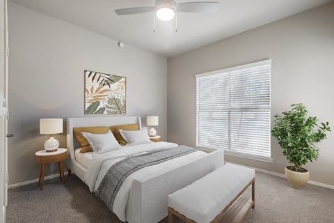 A bedroom with a bed, two lamps, a bench, and a plant.