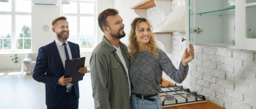 Couple inspecting kitchen cabinets during an apartment tour with a real estate agent, checking key details during peak rental season.