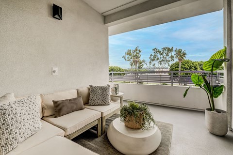 A living room with a white couch and a large window overlooking a balcony.