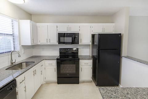 A black refrigerator sits in a kitchen with white cabinets.