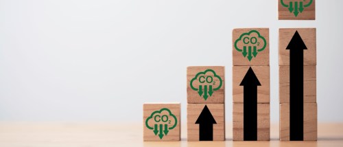 Wooden blocks stacked in a pyramid shape, each marked with green CO2 symbols and black arrows, illustrating the importance of reducing your carbon footprint.