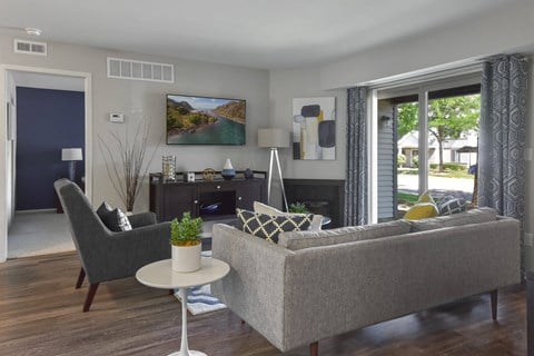 A living room with a grey couch, a grey chair, a white table, and a painting on the wall.