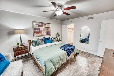 the master bedroom has a large bed and a ceiling fan at Juniper Springs Apartments, Austin, TX