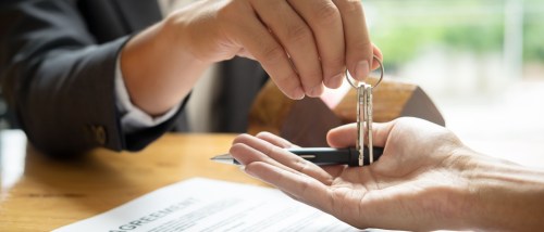 Close-up of a real estate agent handing over house keys to a renter-turned-owner above a signed agreement, after using their right of first refusal.