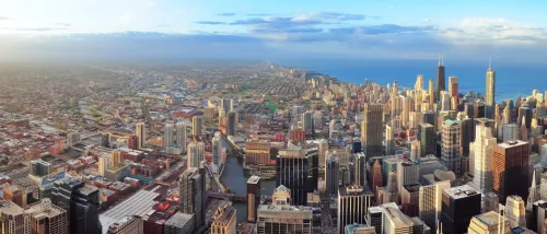 An aerial panorama captures the sprawling urban and suburban landscape of Chicago one of the hottest rental markets in the U.S. at the start of 2025 - showcasing its dense cluster of skyscrapers, including the iconic Willis Tower, transitioning into less concentrated development before meeting the vast expanse of Lake Michigan under a partially clouded sky.