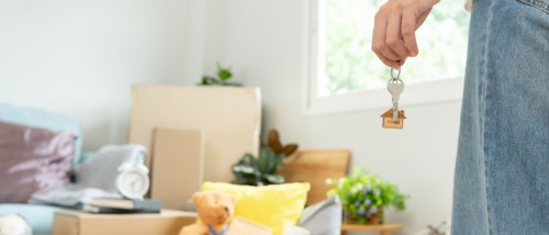 Moving house, relocation. Woman holds key with house keychain in new apartment.