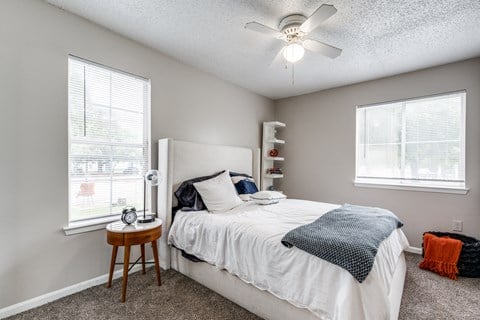 a bedroom with a bed and a ceiling fan and two windows