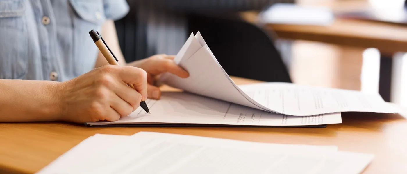 Close up of a person holding a pen and signing a document to illustrate a lease renewal.
