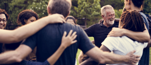A diverse group of individuals embracing while gathering outdoors in a community event, showcasing good neighbor etiquette.